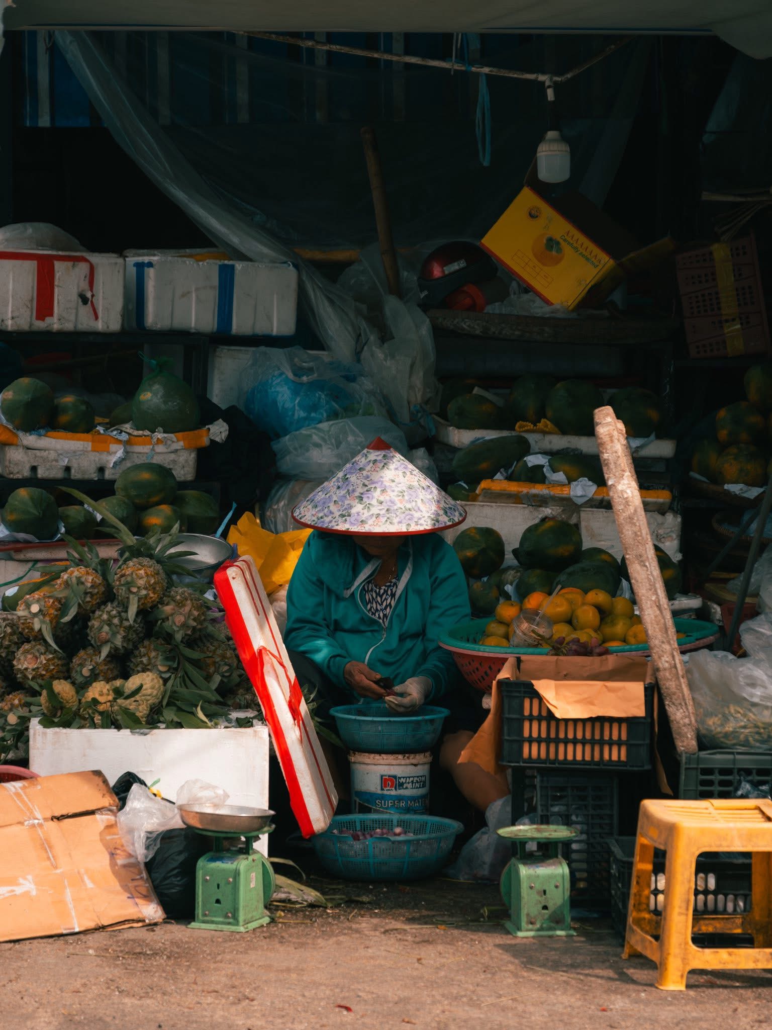 Bà cụ đội nón lá ngồi bán trái cây giữa sạp hàng ở chợ Đông Ba Huế lúc sáng sớm