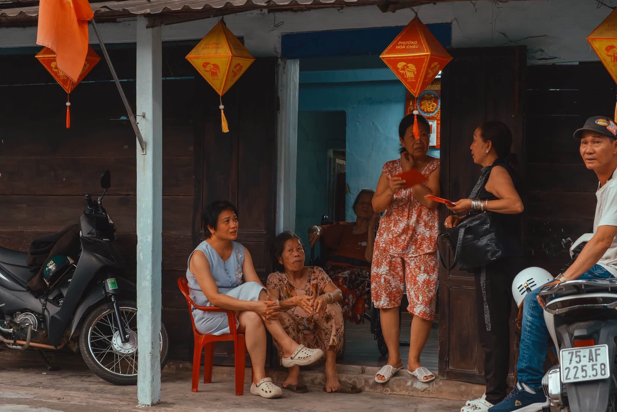 Người dân Bao Vinh ngồi trò chuyện trước hiên nhà gỗ cổ dưới đèn lồng — nếp sống chậm Cố Đô