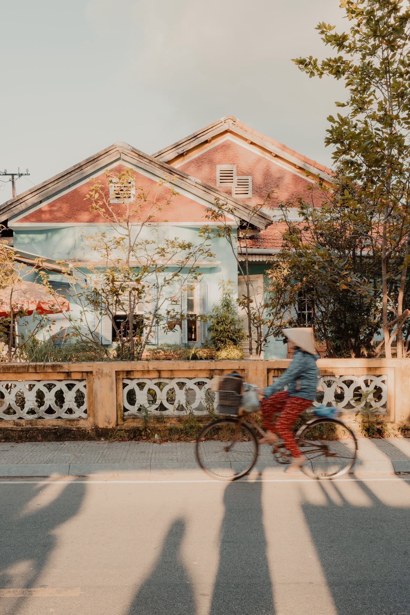 Người phụ nữ đội nón lá đạp xe qua ngôi nhà cũ màu pastel ở Huế