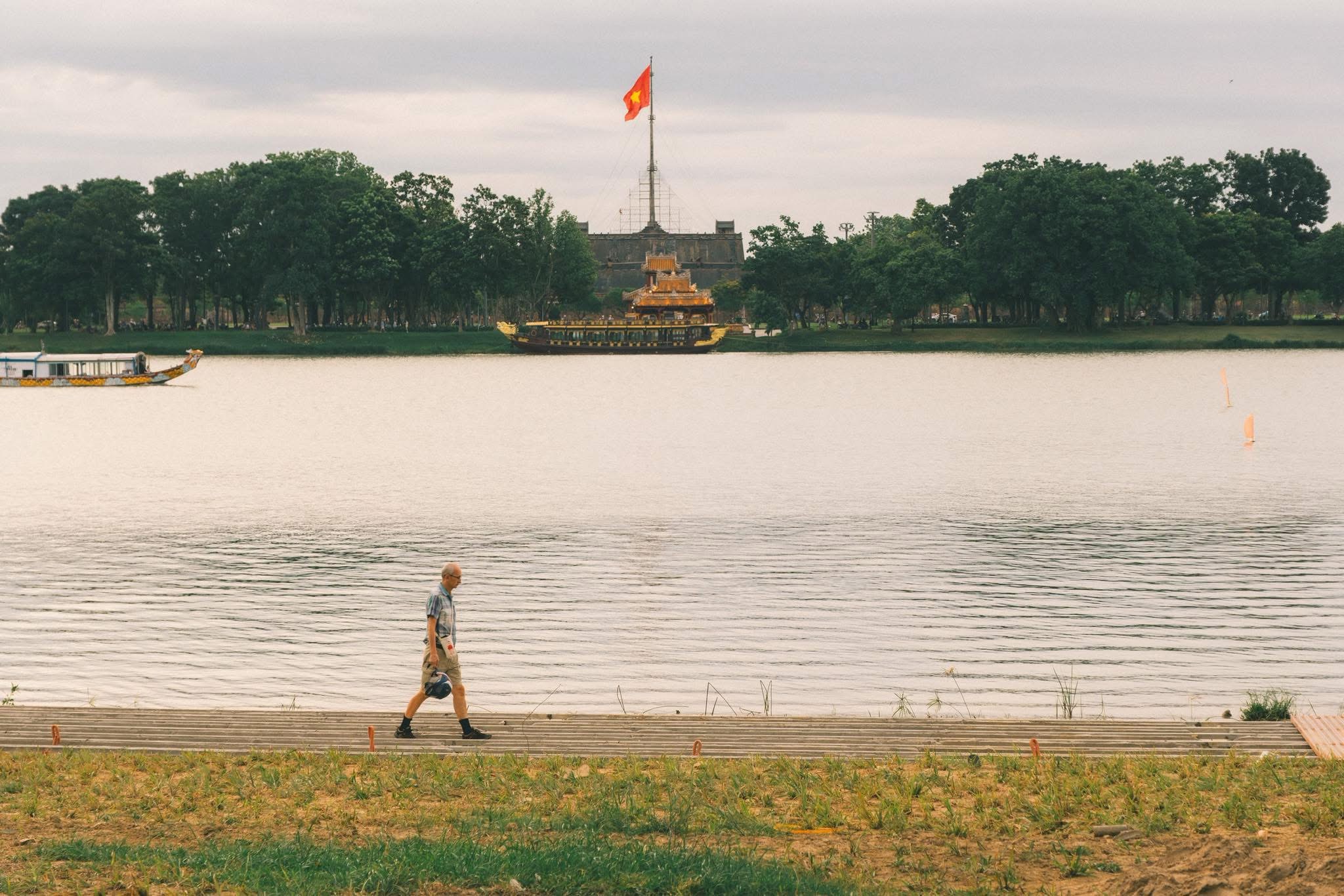 Người đàn ông đi bộ một mình bên sông Hương, phía sau là Kỳ Đài và thuyền rồng Huế